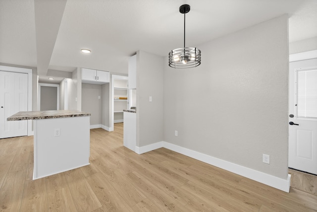 kitchen with white cabinets, light wood-type flooring, and decorative light fixtures