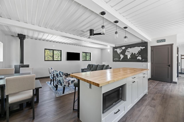 kitchen with a kitchen island, pendant lighting, built in microwave, white cabinetry, and butcher block counters