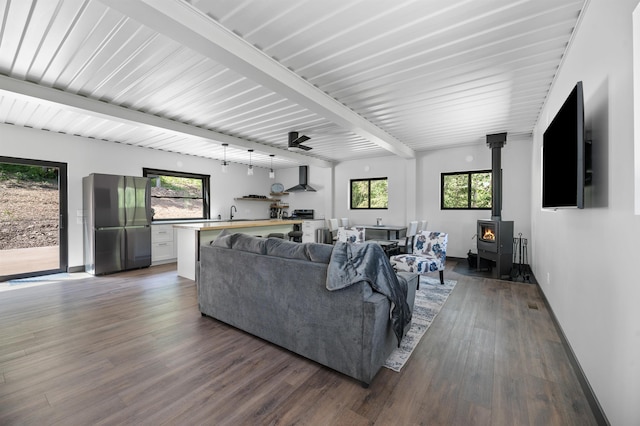 living room with a healthy amount of sunlight, dark hardwood / wood-style flooring, beam ceiling, and a wood stove