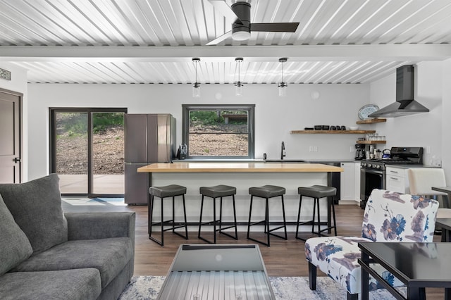 kitchen with a breakfast bar, white cabinetry, hanging light fixtures, appliances with stainless steel finishes, and wall chimney range hood