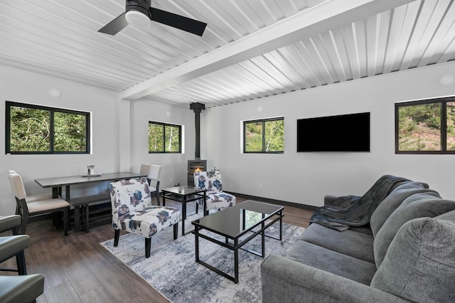 living room featuring dark hardwood / wood-style floors, ceiling fan, beam ceiling, and a wood stove