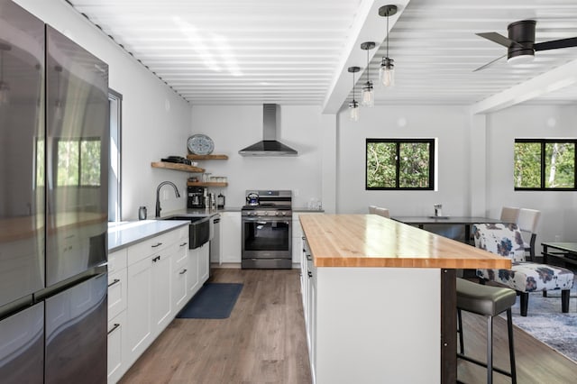 kitchen featuring pendant lighting, butcher block countertops, white cabinets, stainless steel appliances, and wall chimney exhaust hood