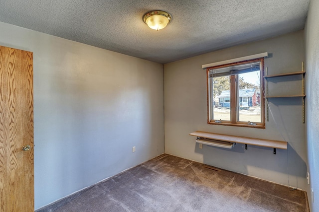 unfurnished room featuring dark carpet and a textured ceiling