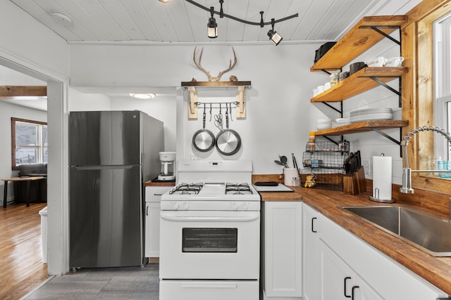 kitchen featuring butcher block counters, sink, white cabinetry, refrigerator, and white gas range oven