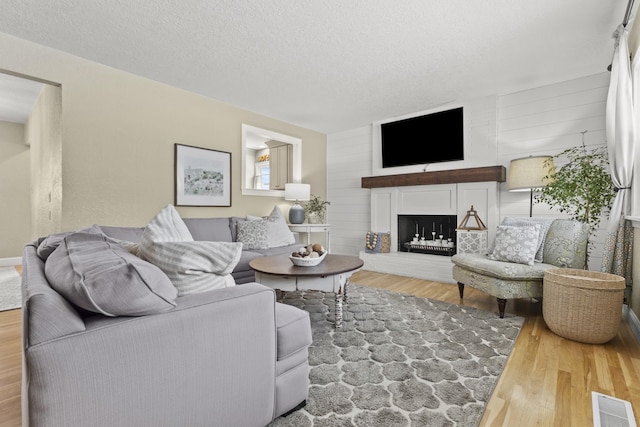 living room featuring wood-type flooring, a large fireplace, and a textured ceiling