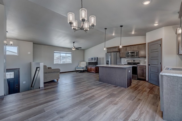 kitchen with vaulted ceiling, appliances with stainless steel finishes, a kitchen island, wood-type flooring, and hanging light fixtures