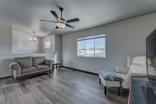 living room featuring vaulted ceiling, ceiling fan with notable chandelier, and light wood-type flooring