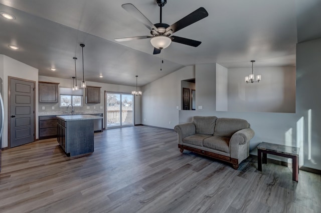 living room with wood-type flooring, vaulted ceiling, sink, and ceiling fan with notable chandelier