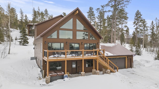 snow covered back of property featuring an attached garage, stairway, and a wooden deck