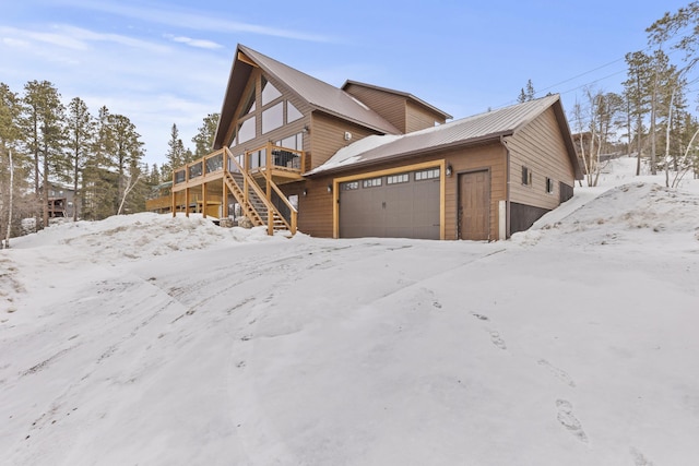 snow covered property with a deck, an attached garage, and stairs