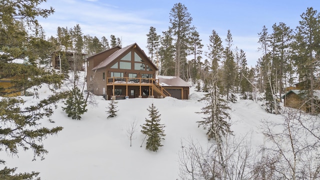 snow covered back of property featuring a garage, stairs, and a deck