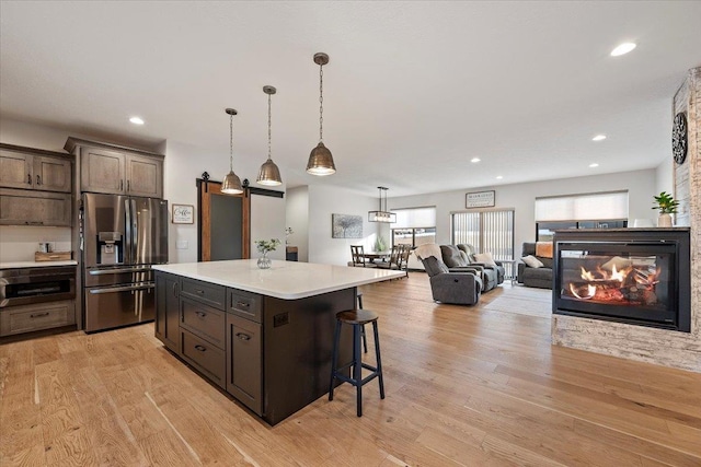 kitchen featuring a breakfast bar, a center island, dark brown cabinetry, stainless steel refrigerator with ice dispenser, and light wood-type flooring