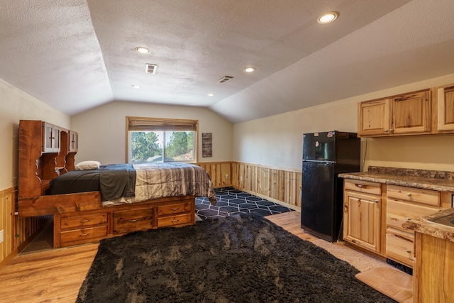 bedroom with black fridge, vaulted ceiling, and a textured ceiling