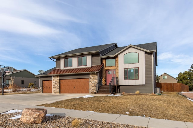 view of front of property featuring concrete driveway, board and batten siding, a standing seam roof, fence, and stone siding