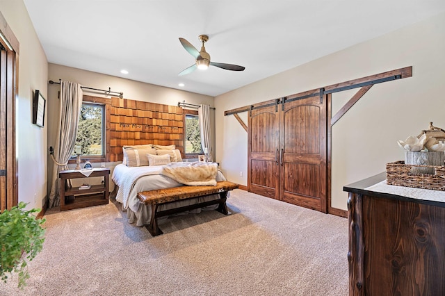 bedroom with ceiling fan, light colored carpet, and a barn door