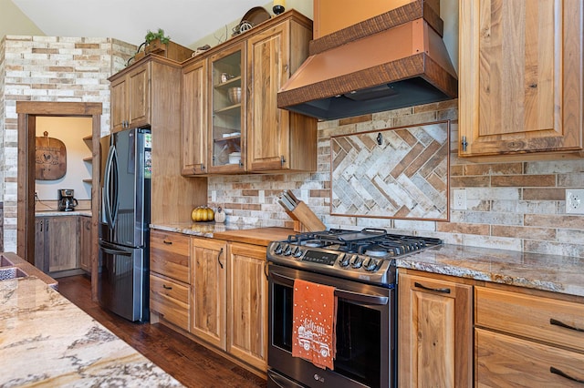 kitchen featuring dark wood-type flooring, custom exhaust hood, light stone counters, appliances with stainless steel finishes, and backsplash