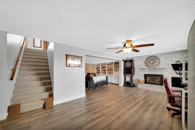 living room featuring ceiling fan, a brick fireplace, hardwood / wood-style floors, and a textured ceiling