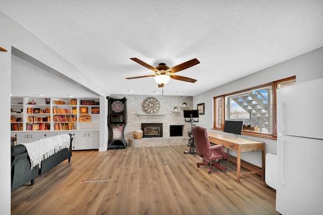 home office with ceiling fan, a fireplace, a textured ceiling, and light hardwood / wood-style floors