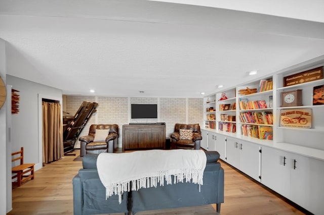 living room with brick wall, light hardwood / wood-style floors, and a textured ceiling