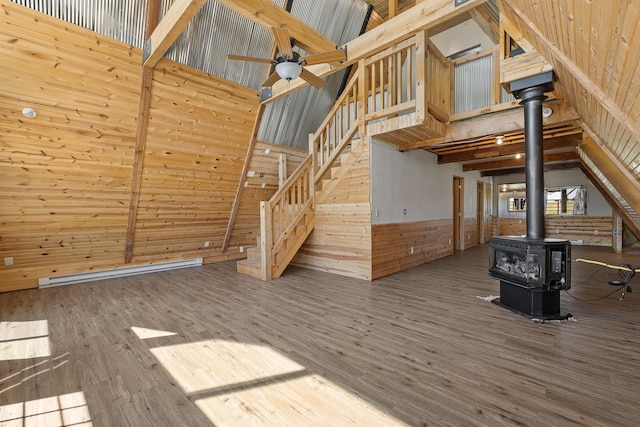 unfurnished living room featuring a wood stove, wooden walls, ceiling fan, hardwood / wood-style floors, and a high ceiling