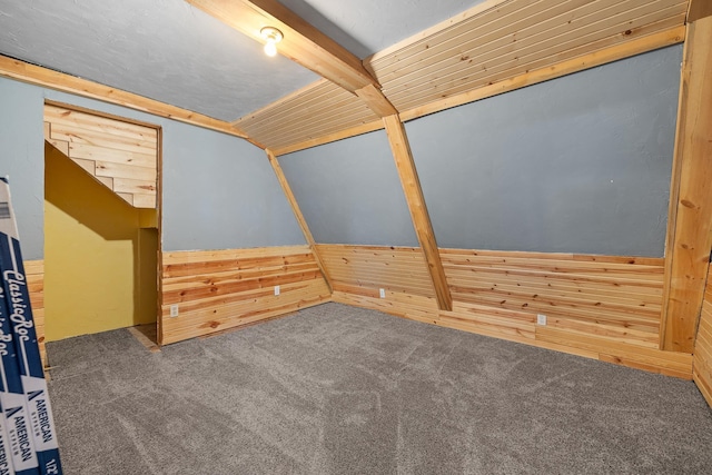 empty room featuring wooden walls, beam ceiling, and dark colored carpet