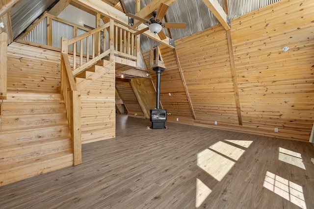 unfurnished living room with a towering ceiling, wood-type flooring, wood walls, and a wood stove