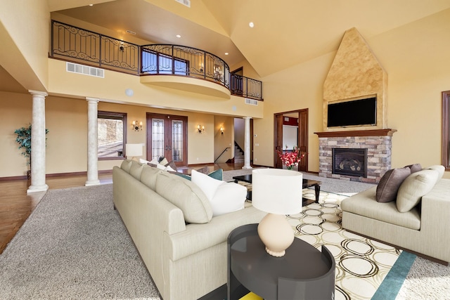 living room featuring a stone fireplace, high vaulted ceiling, decorative columns, light wood-type flooring, and french doors