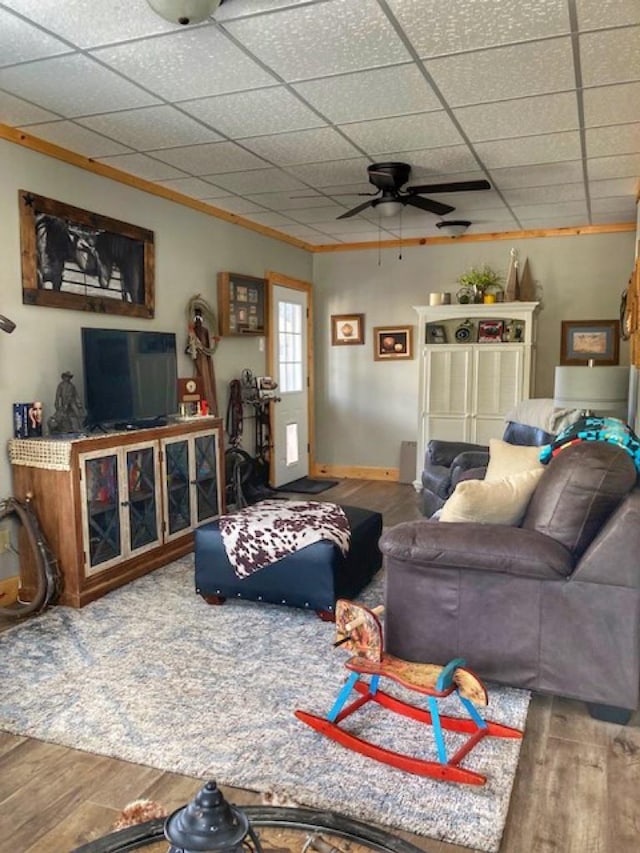 living area with ornamental molding, a drop ceiling, baseboards, and wood finished floors