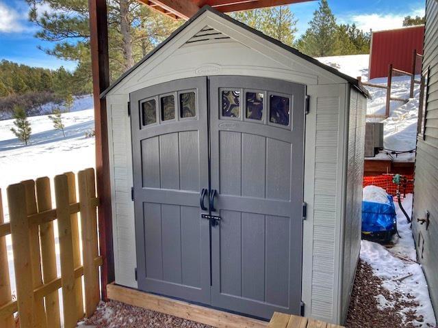 snow covered structure featuring an outbuilding, fence, and a storage unit