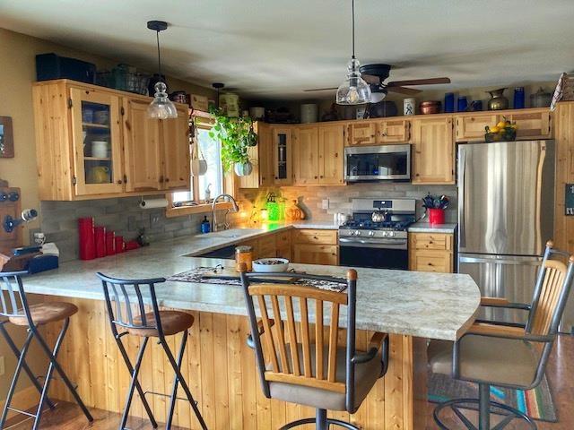 kitchen featuring a breakfast bar area, light countertops, appliances with stainless steel finishes, glass insert cabinets, and a sink