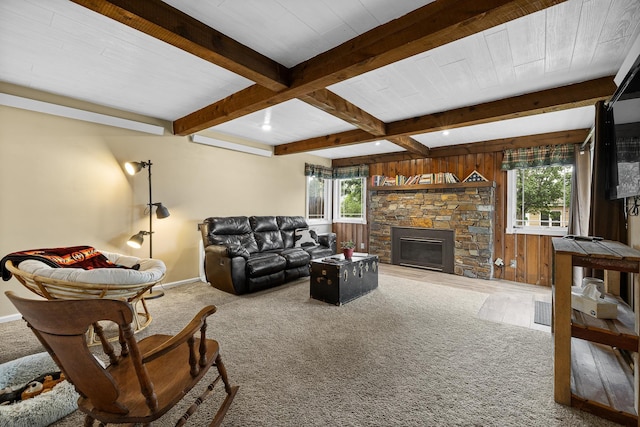 living room featuring a stone fireplace, beamed ceiling, wooden walls, and baseboards