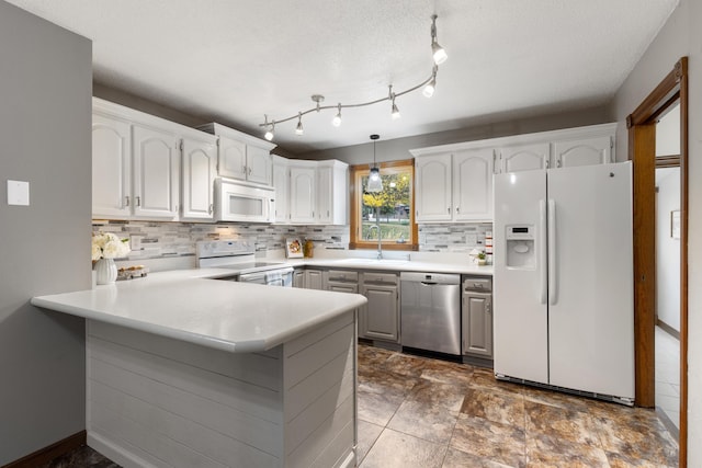 kitchen with a peninsula, white appliances, hanging light fixtures, and white cabinets