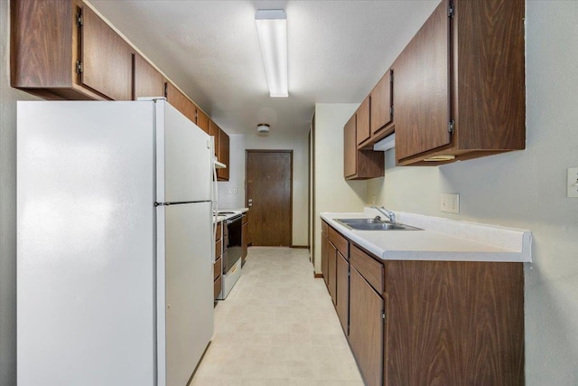 kitchen with electric range oven, freestanding refrigerator, light countertops, light floors, and a sink