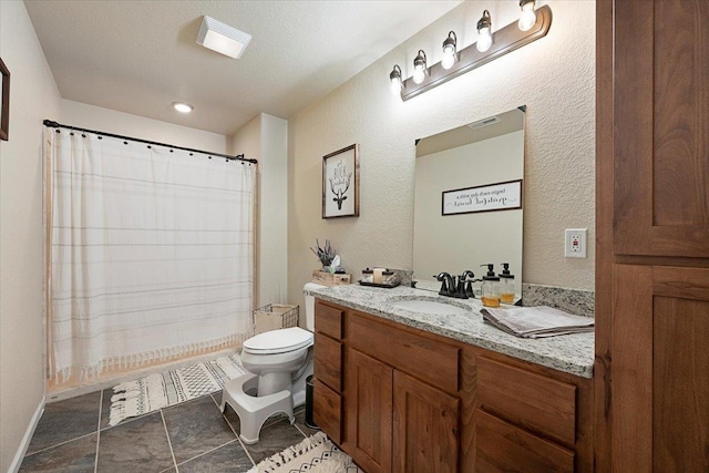 bathroom featuring a textured wall, curtained shower, vanity, and toilet