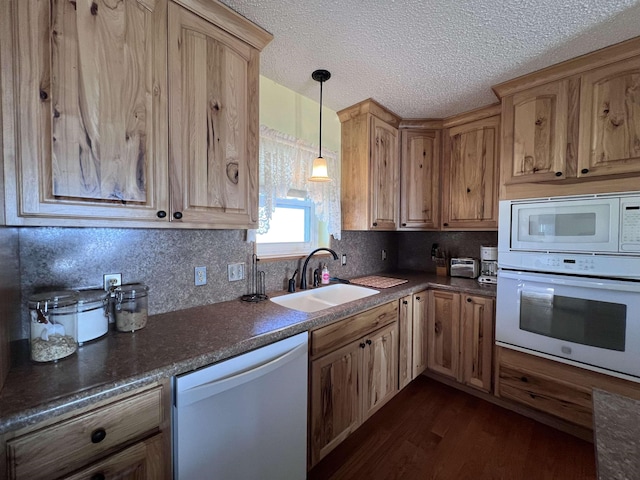 kitchen with dark countertops, white appliances, pendant lighting, and a sink