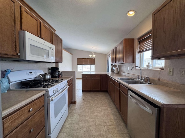 kitchen with pendant lighting, a notable chandelier, vaulted ceiling, a sink, and white appliances