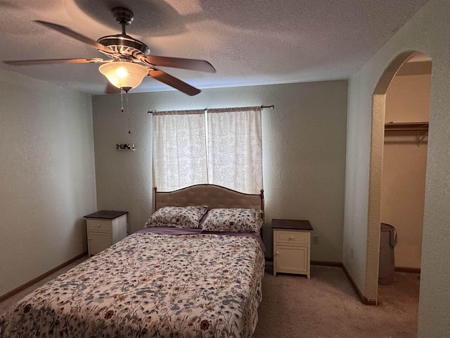 bedroom featuring baseboards, arched walkways, light colored carpet, a textured wall, and a textured ceiling