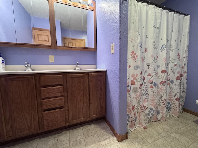 full bathroom with double vanity, a sink, and baseboards