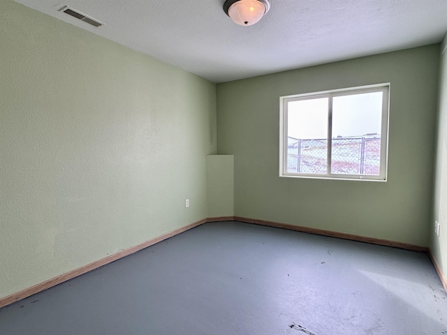 empty room with visible vents, a textured wall, a textured ceiling, concrete flooring, and baseboards