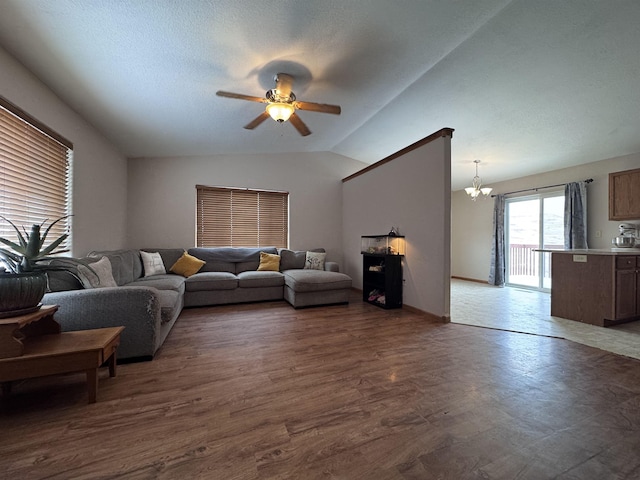 living room with a textured ceiling, vaulted ceiling, dark wood finished floors, and ceiling fan with notable chandelier