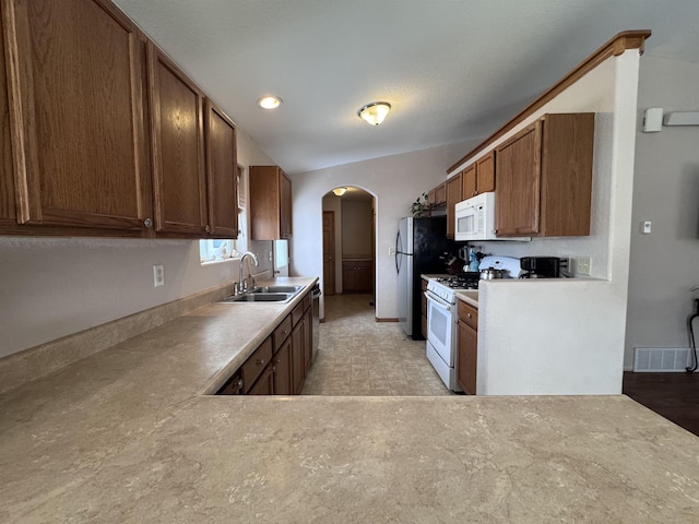 kitchen featuring arched walkways, white appliances, a sink, light countertops, and brown cabinets