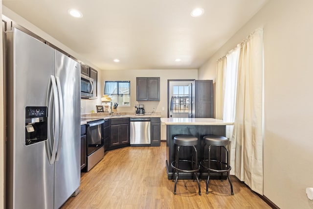 kitchen with light wood finished floors, appliances with stainless steel finishes, a breakfast bar area, light countertops, and recessed lighting