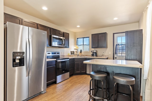 kitchen featuring light wood finished floors, light countertops, appliances with stainless steel finishes, dark brown cabinetry, and a kitchen bar