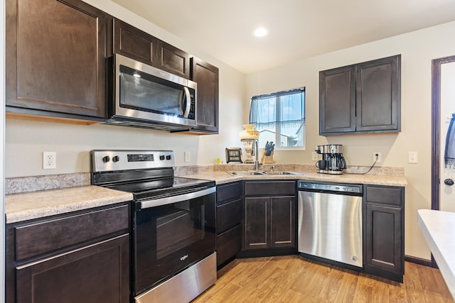 kitchen with stainless steel appliances, light countertops, dark brown cabinetry, a sink, and light wood-type flooring