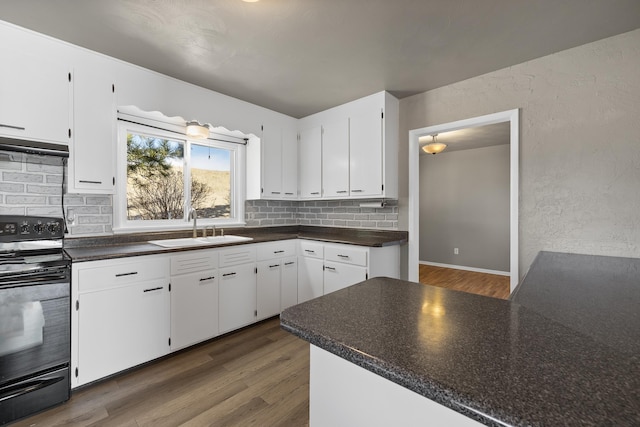 kitchen with black electric range, dark countertops, a sink, and white cabinetry