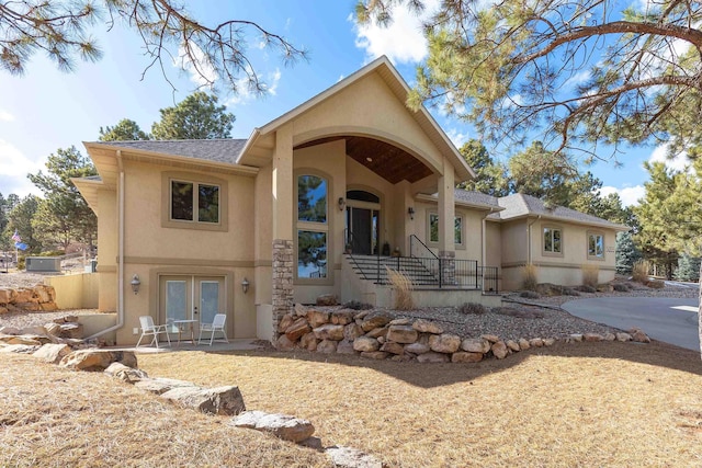 view of front facade featuring stucco siding, roof with shingles, a patio, and french doors