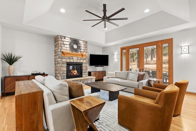 living room with light wood-type flooring, a raised ceiling, a fireplace, and recessed lighting