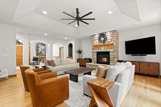 living area with a tray ceiling, a stone fireplace, light wood finished floors, and recessed lighting