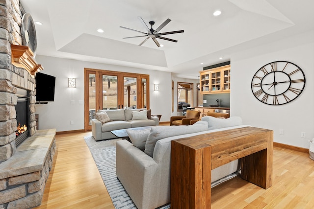 living room featuring light wood-style flooring, ceiling fan, a tray ceiling, a fireplace, and recessed lighting