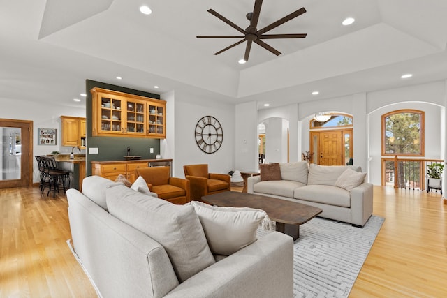 living area with arched walkways, light wood finished floors, a raised ceiling, and recessed lighting